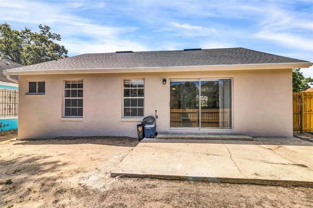 back of house featuring stucco siding, fence, roof with shingles, and a patio