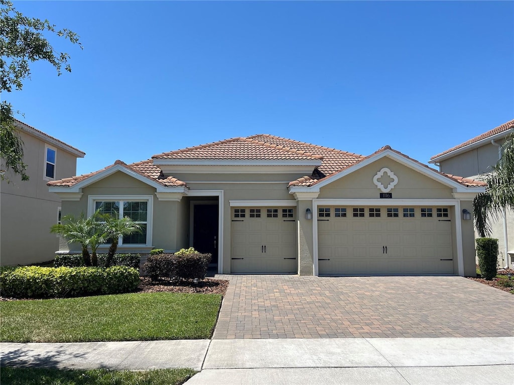 view of front facade with a tile roof, decorative driveway, a front lawn, a garage, and stucco siding