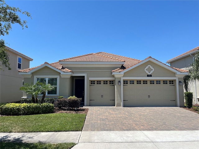 view of front facade with a tile roof, decorative driveway, a front lawn, a garage, and stucco siding
