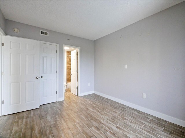 6165 Carrier Dr Unit 1603, Orlando, FL 32819 - unfurnished bedroom featuring baseboards, light wood-style floors, a closet, ensuite bath, and a textured ceiling