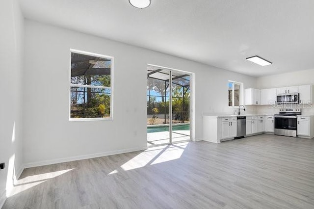 227 Sand Ridge Dr, Davenport, FL 33896 - kitchen with white cabinets, stainless steel appliances, baseboards, light wood-style floors, and light countertops