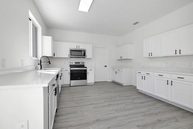 227 Sand Ridge Dr, Davenport, FL 33896 - kitchen featuring white cabinets, stainless steel appliances, visible vents, a sink, and light wood-style floors