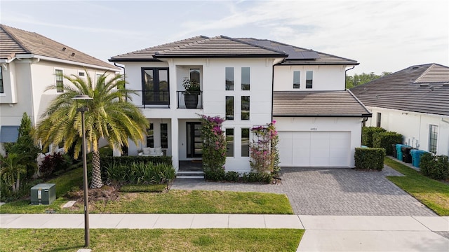 view of front of home with a garage, stucco siding, decorative driveway, a balcony, and a tiled roof
