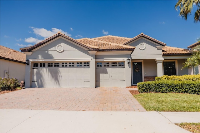 view of front of property featuring a tiled roof, stucco siding, an attached garage, and decorative driveway