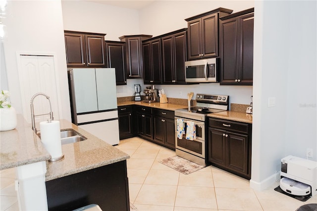 kitchen with light tile patterned flooring, dark brown cabinets, light stone countertops, a sink, and appliances with stainless steel finishes