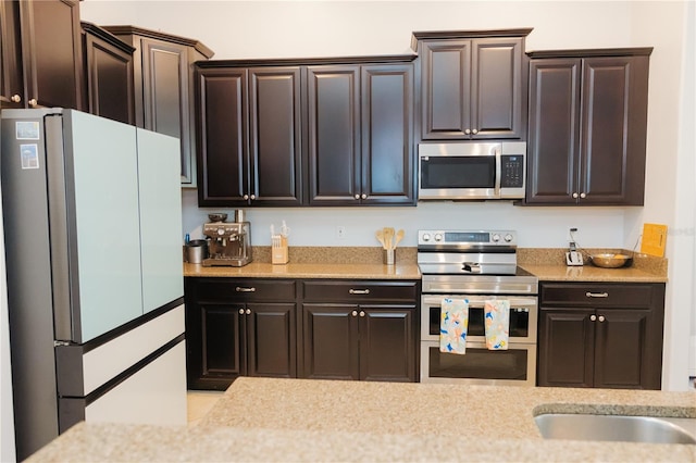 kitchen with a sink, light stone countertops, stainless steel appliances, and dark brown cabinets
