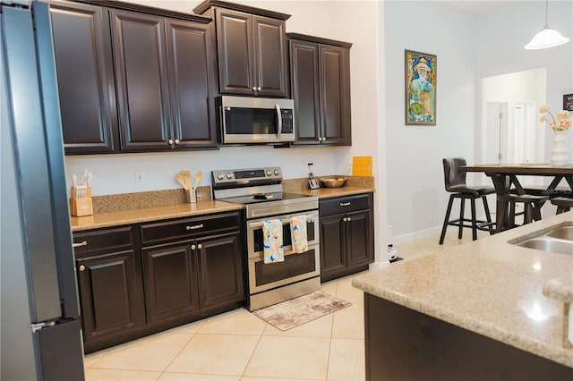 kitchen with light tile patterned flooring, appliances with stainless steel finishes, light stone counters, baseboards, and pendant lighting