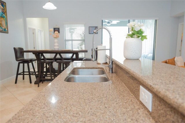kitchen featuring baseboards, light stone counters, a sink, light tile patterned floors, and hanging light fixtures