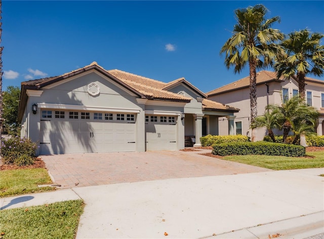 view of front of home with decorative driveway, a garage, a tile roof, and stucco siding