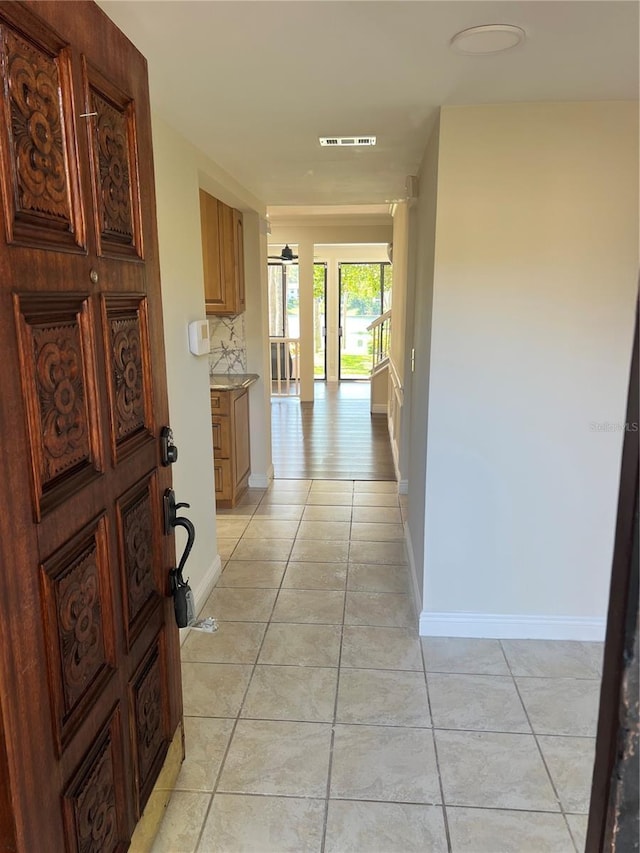 hallway with baseboards, visible vents, and light tile patterned floors