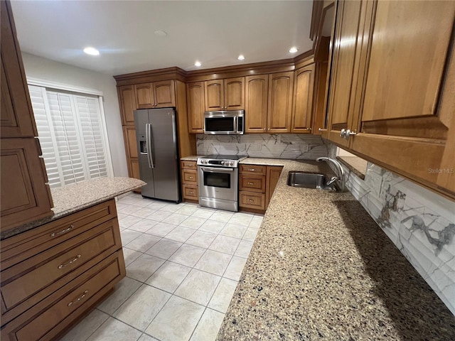 kitchen with light stone counters, a sink, brown cabinetry, stainless steel appliances, and backsplash