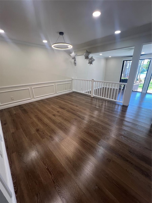 spare room with wainscoting, a decorative wall, ornamental molding, and dark wood finished floors