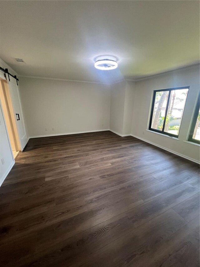unfurnished room with a barn door, visible vents, crown molding, baseboards, and dark wood-style flooring