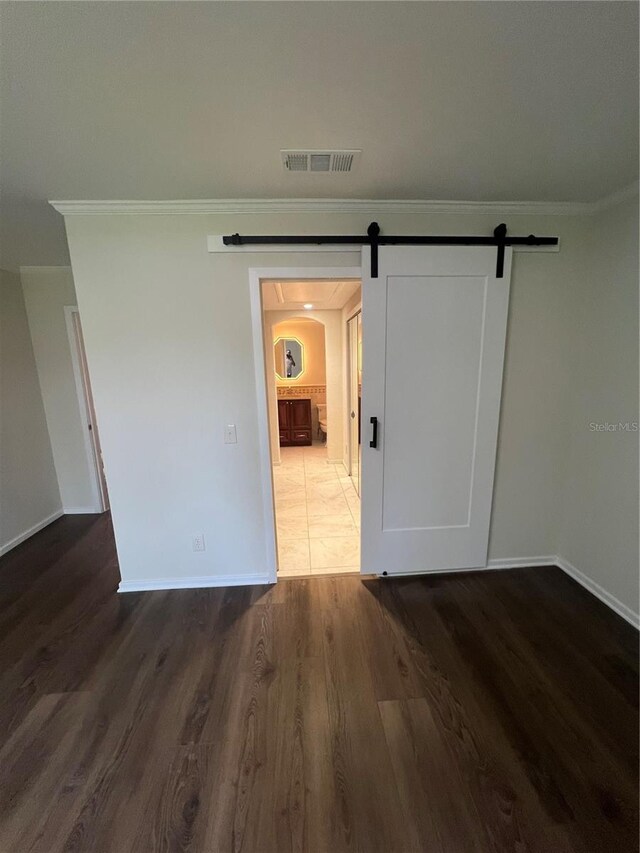 spare room with wood finished floors, baseboards, ornamental molding, and a barn door