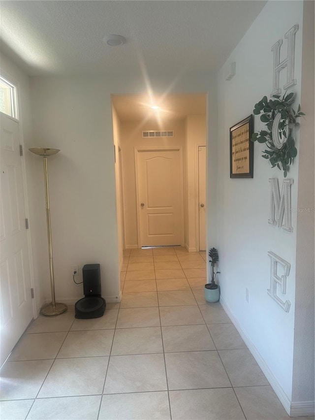 hallway featuring light tile patterned flooring, visible vents, and baseboards