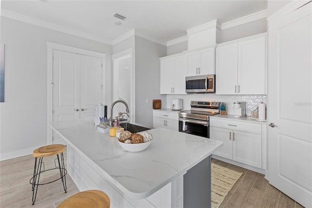 kitchen featuring appliances with stainless steel finishes, a sink, light wood-style floors, a breakfast bar area, and white cabinetry