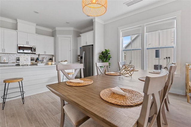 dining space with light wood-style floors, a chandelier, and ornamental molding