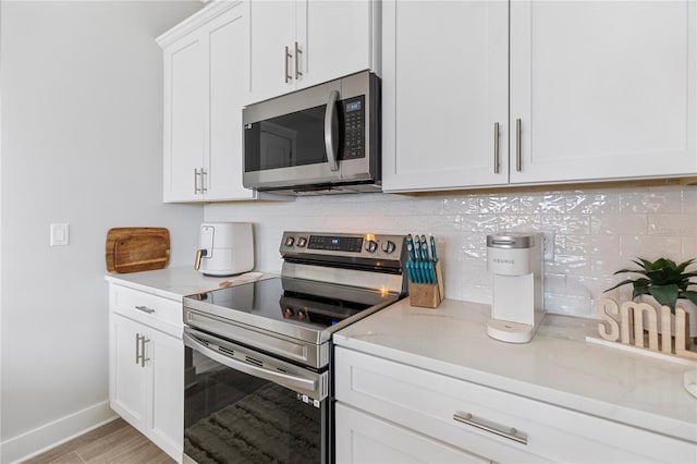 kitchen featuring stainless steel appliances, backsplash, baseboards, light wood-style flooring, and white cabinets