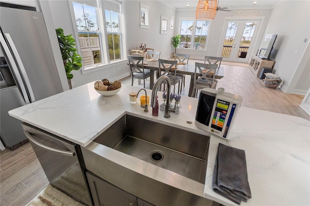 kitchen with a sink, light wood-type flooring, stainless steel appliances, french doors, and baseboards