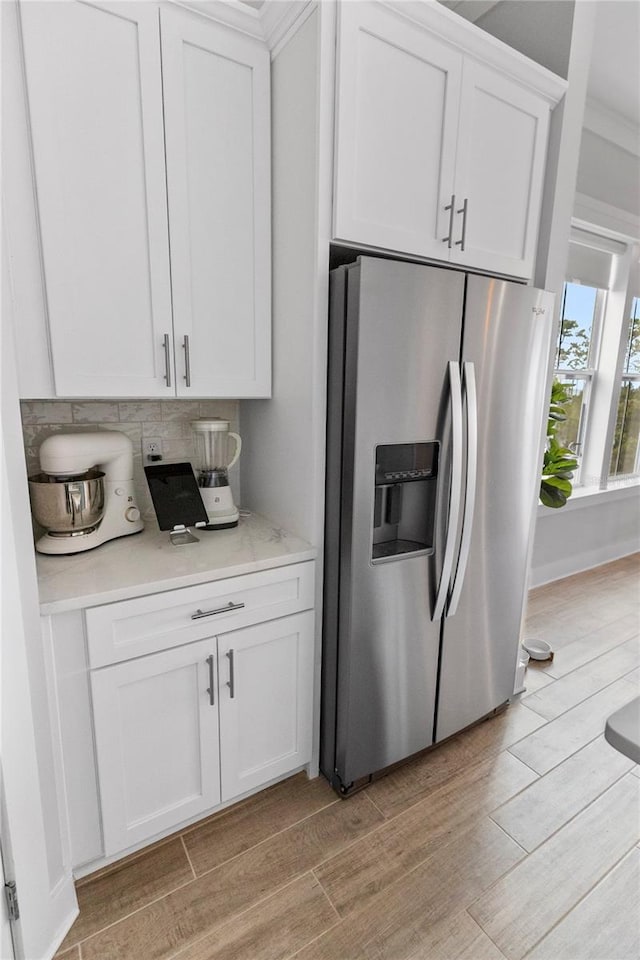 kitchen featuring stainless steel fridge, light wood-type flooring, light countertops, white cabinets, and tasteful backsplash