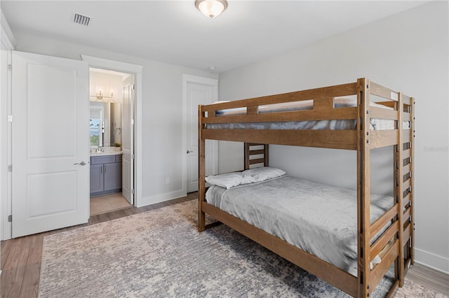 bedroom with light wood finished floors, baseboards, and ensuite bath