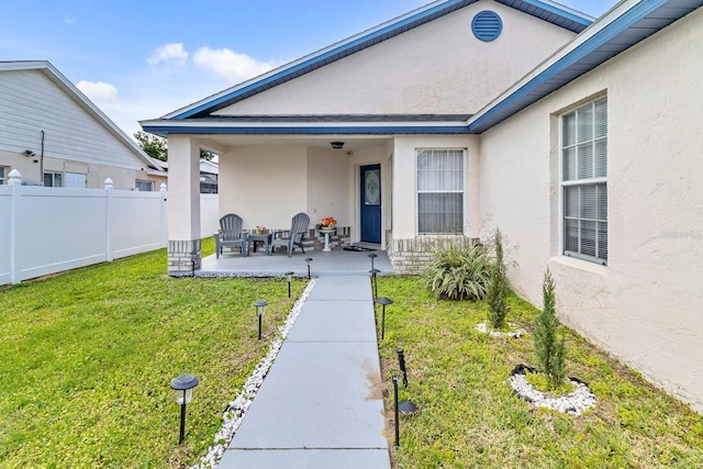 property entrance featuring fence, a lawn, a patio area, and stucco siding