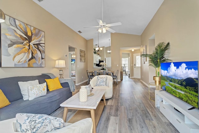 living room with vaulted ceiling, visible vents, light wood-style floors, baseboards, and ceiling fan with notable chandelier