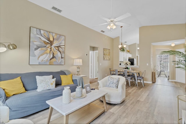 living area featuring light wood-type flooring, visible vents, lofted ceiling, and ceiling fan with notable chandelier