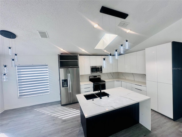 kitchen with a sink, a textured ceiling, light wood-type flooring, modern cabinets, and appliances with stainless steel finishes