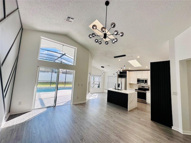 kitchen with a notable chandelier, a textured ceiling, an island with sink, light countertops, and appliances with stainless steel finishes