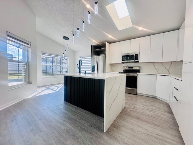kitchen featuring a sink, lofted ceiling with skylight, light wood-style floors, modern cabinets, and stainless steel appliances