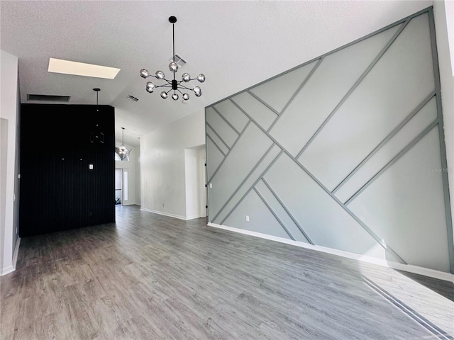 unfurnished living room with a textured ceiling, lofted ceiling with skylight, baseboards, an inviting chandelier, and wood finished floors