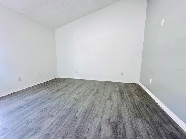spare room featuring vaulted ceiling, wood finished floors, and baseboards