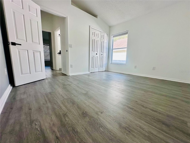 unfurnished bedroom featuring vaulted ceiling, wood finished floors, a textured ceiling, and baseboards
