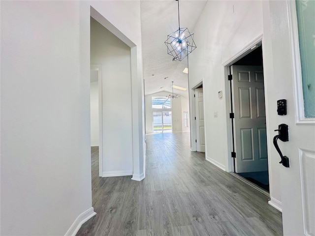 hallway featuring lofted ceiling, wood finished floors, baseboards, and an inviting chandelier