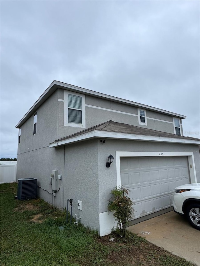 view of side of home with fence, cooling unit, concrete driveway, stucco siding, and a garage