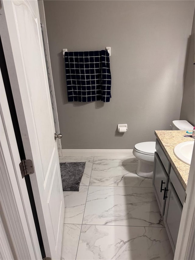 bathroom featuring toilet, vanity, marble finish floor, and baseboards