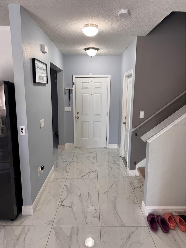 foyer entrance featuring marble finish floor, stairs, a textured ceiling, and baseboards