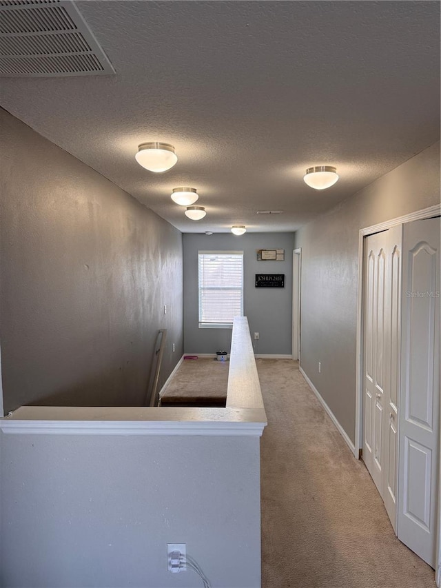 hall featuring a textured ceiling, visible vents, baseboards, and light carpet