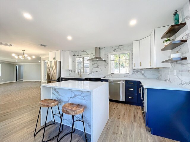 905 W 11th Ave, Mount Dora, FL 32757 - kitchen featuring appliances with stainless steel finishes, blue cabinets, open shelves, wall chimney range hood, and a kitchen bar