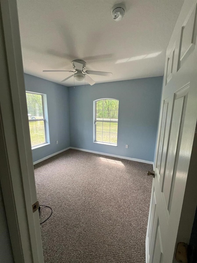 carpeted spare room with ceiling fan and baseboards