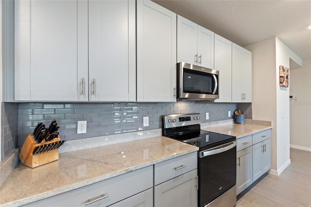 kitchen with tasteful backsplash, light wood-style floors, stainless steel appliances, baseboards, and light stone countertops