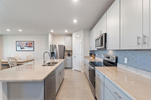 kitchen featuring recessed lighting, light stone countertops, a sink, backsplash, and appliances with stainless steel finishes