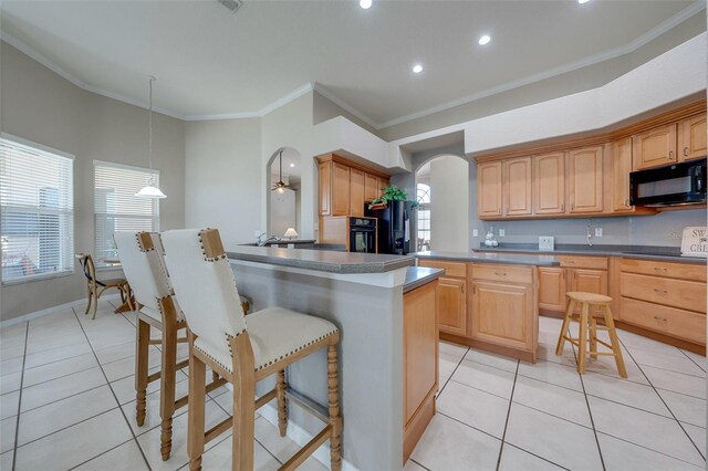 kitchen with a breakfast bar area, arched walkways, black appliances, crown molding, and light tile patterned floors