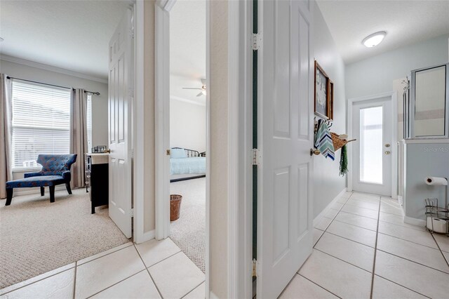 hallway featuring light carpet, a wealth of natural light, light tile patterned floors, and crown molding