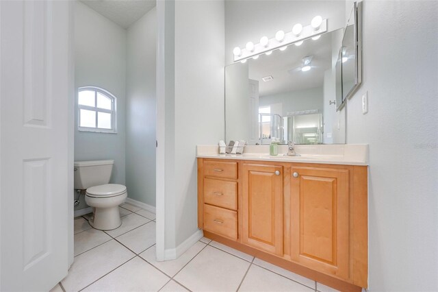 bathroom with tile patterned flooring, toilet, vanity, baseboards, and ceiling fan