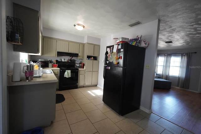 kitchen featuring extractor fan, black appliances, cream cabinets, light countertops, and visible vents