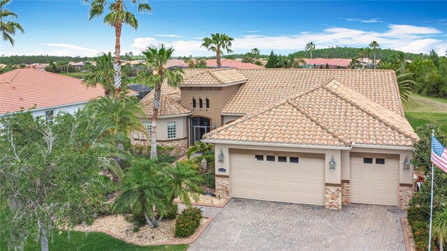 mediterranean / spanish-style home with a garage, stone siding, decorative driveway, stucco siding, and a tiled roof