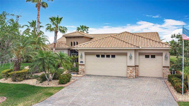 mediterranean / spanish house with a garage, stucco siding, decorative driveway, and stone siding