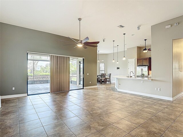 unfurnished living room with visible vents, a sink, a towering ceiling, baseboards, and a ceiling fan